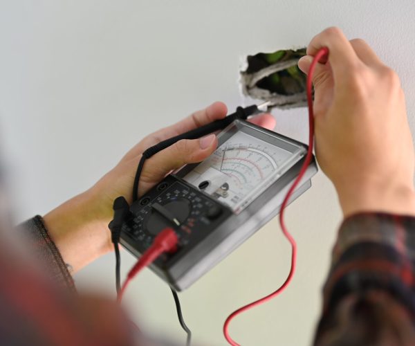 Electrician installer using a multimeter to test power line current in an electrical system on construction site.