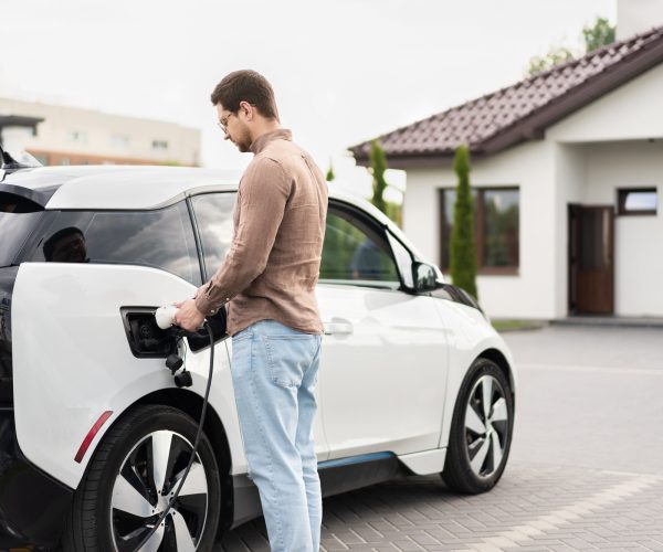 Man Charging Electric Car at Home on a Sunny Day