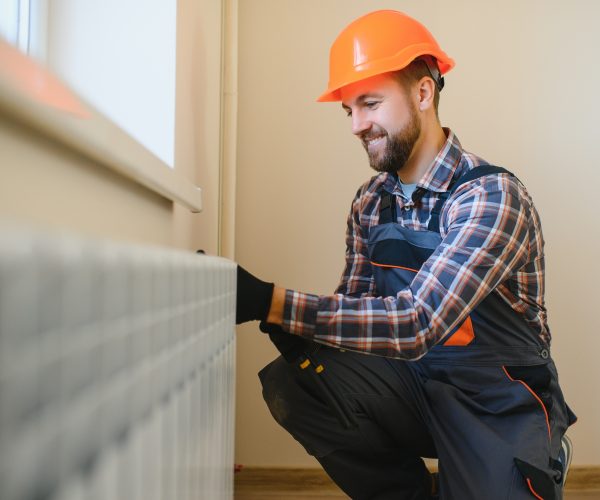 Plumber man is blocking repairs radiators of heating battery in apartment tap